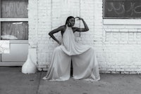 a woman in a white jumpsuit leaning against a brick wall