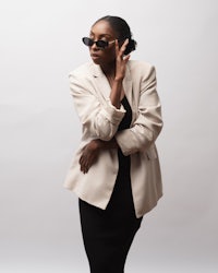 a black woman in a blazer and sunglasses posing on a white background